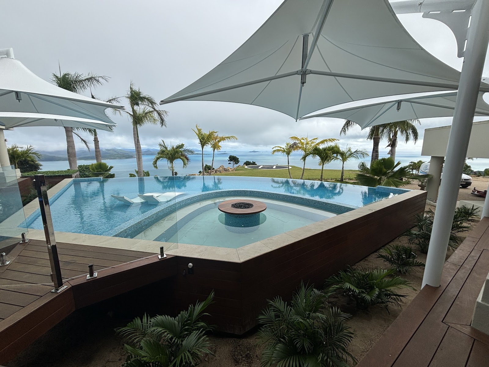 Resort pool with shade sails and a fire pit island by the ocean